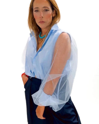 Woman wearing a light blue sheer blouse over a dark blue dress with a white background